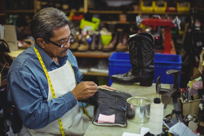 Shoemaker applying glue on shoe in workshop